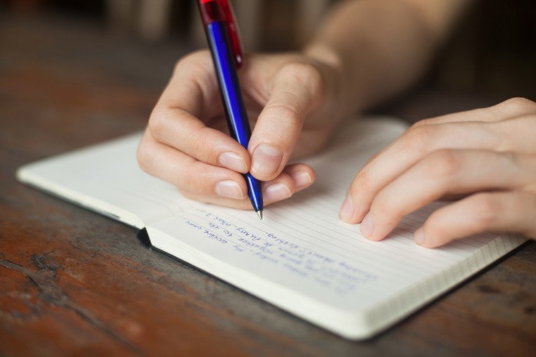 un baiat care scrie intr-un jurnal pe o masa de lemn